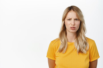 Fototapeta premium Dislike and aversion. Young woman grimaces and look with disgust at smth bad, stands over white background