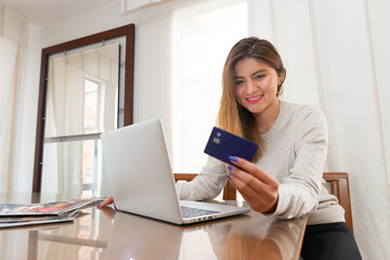 Fototapeta premium happy young caucasian girl looking at the credit card on her left hand before shopping online at home. High quality photo