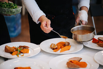 Cook plating chicken breast with carrot and finishing with some sauce from the pan. No face.