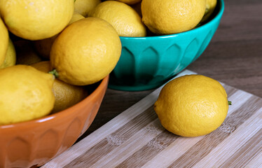 One lemon on cooking board, many lemons fresh in orange and blue bowls