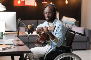 African man with disability sitting in wheelchair and playing guitar during live broadcasting in...