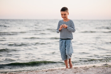Fototapeta na wymiar summer vacation at sea. Boy at seaside. Child collect shells on beach having fun during summer holiday in Ukraine Koblebo. happy kid playing at sunset time. Travel and adventure concept