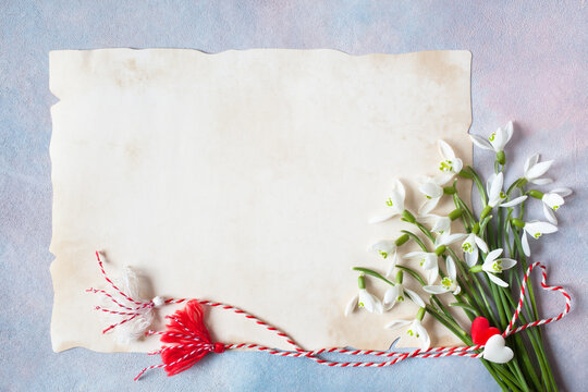 A bouquet of spring flowers of snowdrops and a red-white cord with tassels and hearts, martenitsa symbol, paper for congratulations text on a colorful background. Postcard for the holiday in March 1.