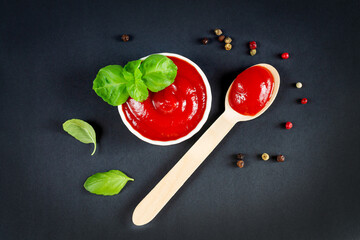 Bowl of ketchup and spoon of red tomato sauce on black kitchen table