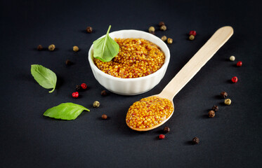 Bowl of french grainy mustard and spoon of dijon mustard on black background