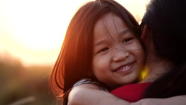 Close-up portrait Asian little child girl embrace or hugging mother, happy, smiling in beautiful nature outdoor sunset or sunshine, slow motion. Concept of love, happy family, mother, kid, summer.