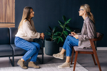 A young female client is discussing with a psychologist while sitting on a couch in a workshop.
