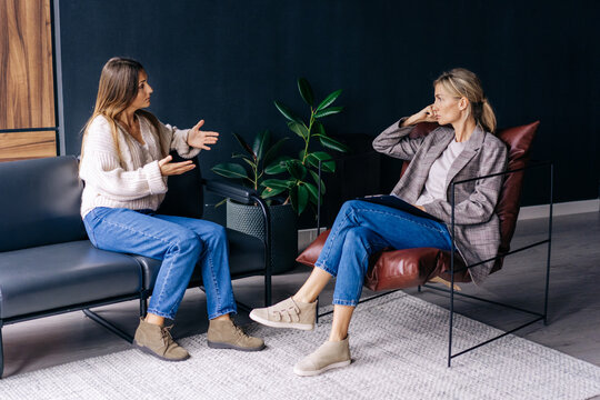 A woman psychologist sitting in a chair listens attentively to a woman talking about problems.