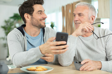 excited elderly dad and grown-up son browsing internet on smartphone