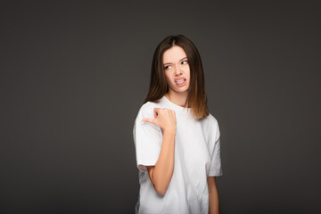 young woman feeling disgusted, sticking out tongue and pointing with thumb isolated on dark grey