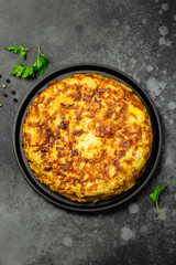 Spanish tortilla with ham and olives in cast iron skillet, dark background. Space for text, top view.