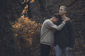 Two tall strong friends are chatting and walking in the forest. Guys have sad communicating with...