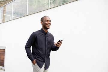smiling African American man walking with phone by white wall