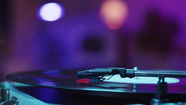 Vinyl record close-up. Vintage old vinil black phonograph spinning. Retro music player on living room home background in evening, pink neon light.
