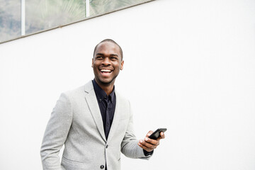 Obraz na płótnie Canvas handsome African American business man smiling with phone by white wall