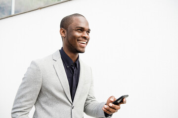 handsome African American business man smiling with mobile phone by white wall