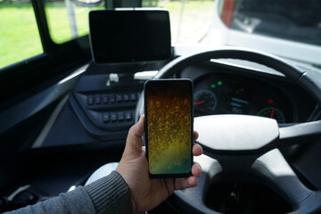 male hand holding smartphone with black mockup on screen, background of car steering wheel. public...