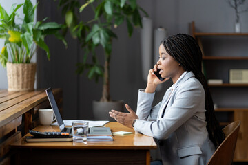 African-american businesswoman in formal outfit using mobile phone, making phonecall in workplace,...