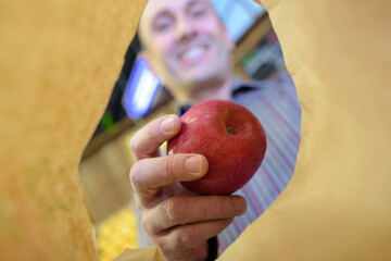 View from paper bag of man holding apple