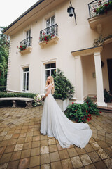 Bride in perfect wedding dress posing against luxury house with wedding boquet.