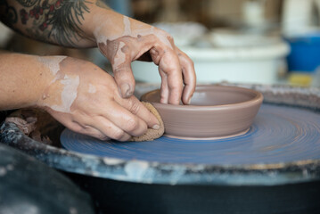 Hands forming a piece of clay on a pottery wheel