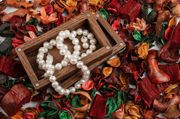 Pearl jewelry in wooden box on dry flowers background.