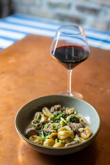 A bowl of gnocchi with steak served with a glass of red wine