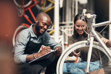 Can I have your details please. Shot of a handsome young man crouching outside his bicycle shop and assisting a customer.