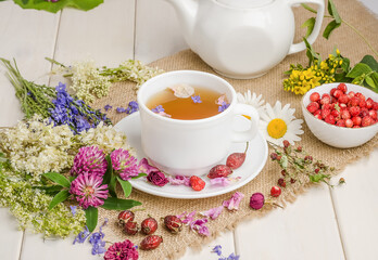 Herbal tea with rosehip, chamomile and clover in a white cup on a wooden table with flowers