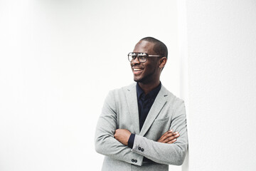 smiling african american businessman leaning against wall with eyeglasses and arms crossed