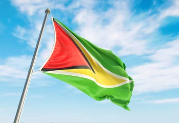 Fotobehang 3d rendering Guyana flag waving in the wind on flagpole. Perspective wiev Guyana flag waving a blue cloudy sky © Adil