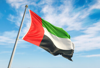United Arab Emirates flag waving in the wind on flagpole. United Arab Emirates flag waving a blue cloudy sky