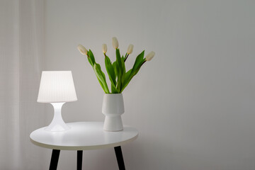 White tulips in a white vase on a table with a table lamp