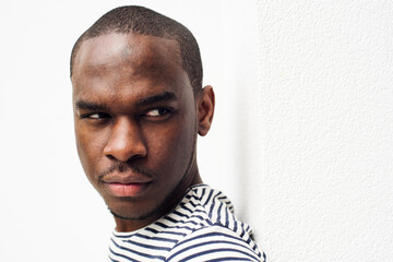 side portrait serious african american man leaning against white wall and glancing