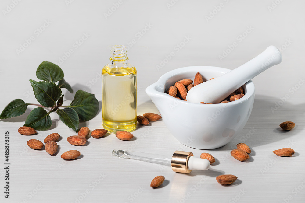 Wall mural Almond oil in a bottle, pipette, bowl with almond kernels on a light background, natural organic cosmetic oil