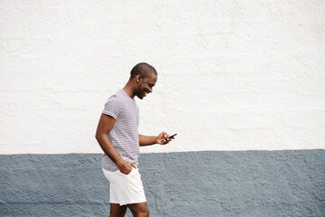 Profile of african american mania t-shirt and shorts walking with cellphone