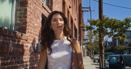 Smiling girl walking near brick wall closeup. Asian pretty lady going on street.