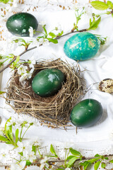 Fototapeta na wymiar Easter egg colored with nettles in green color in nest on table with white tablecloth and decorated with flowering cherry branches, egg colored in vivid mint color, Easter holiday table décor