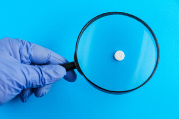 Classic medical pill with risk, doctor's hand in gloves and magnifying glass in blurred foreground....