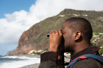 african american man by seaside looking through binoculars