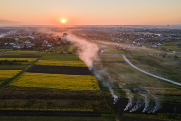 Aerial view of agricultural waste bonfires from dry grass and straw stubble burning with thick smoke polluting air during dry season on farmlands causing global warming and carcinogen fumes