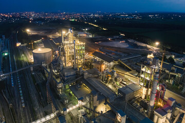 Aerial view of cement factory with high concrete plant structure and tower cranes at industrial production area at night. Manufacture and global industry concept