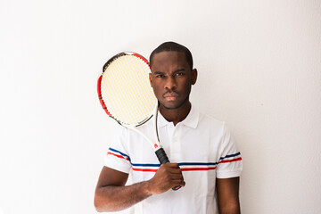 handsome tennis player holding racket by white wall