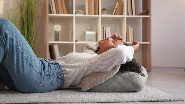 Home relax. Rest indoors. Lazy weekend. Peaceful serene cheerful young woman lying on floor comfortable pillows at cozy living room.