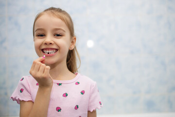 Girl child shows her mouth without one lost milk tooth and smiles. A child in the bathroom holds a...