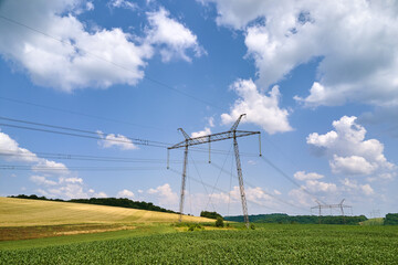 High voltage tower with electric power lines between green agricultural fields. Transfer of electricity concept