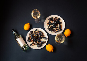 Plates with mussels, bottle of white wine and glasses of white wine on dark background.