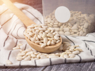 white beans in a wooden cup and spoon are scattered on the table