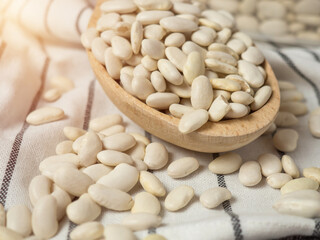 white beans in a wooden cup and spoon are scattered on the table