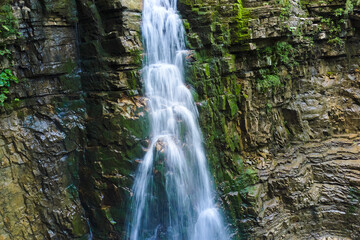 Obraz premium Waterfall on mountain river with white foamy water falling down from rocky formation in summer forest